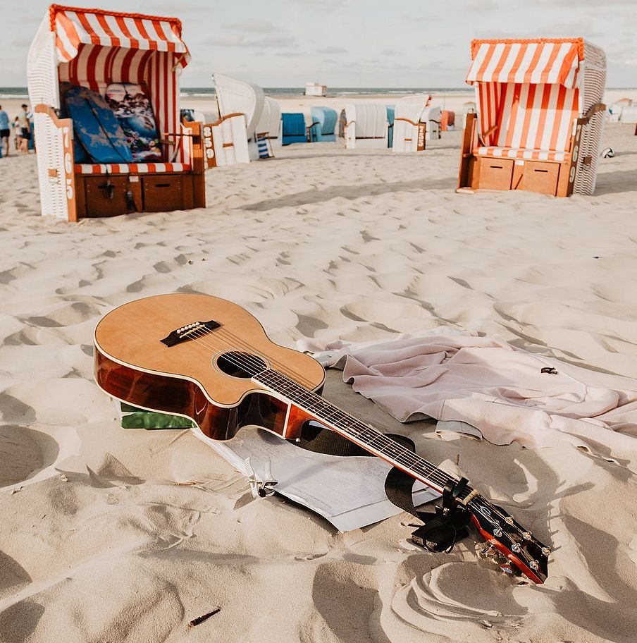 Zdjęcie przedstawia gitarę leżącą na plaży nad morzem.